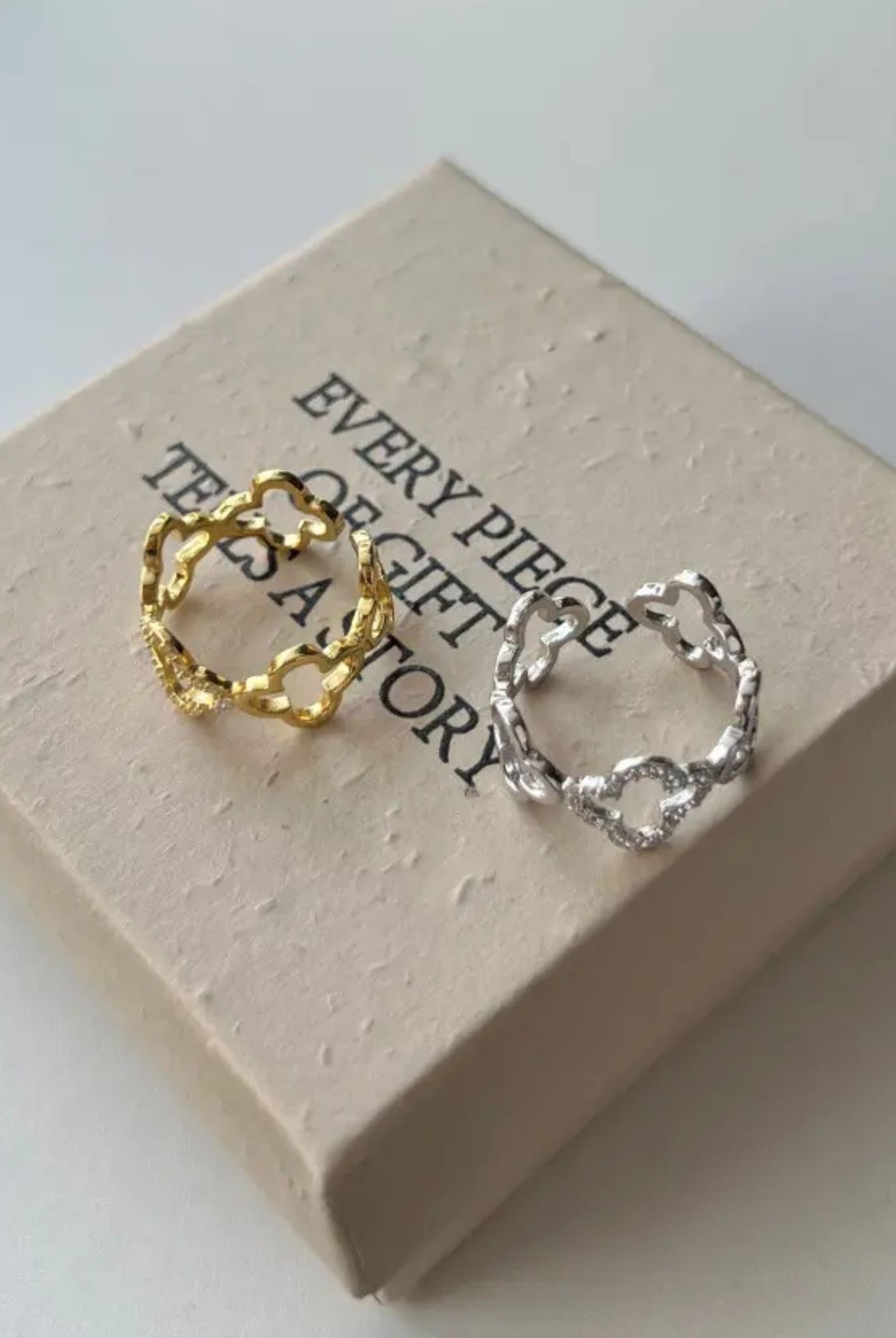 Silver and gold Celeste Clover Rings displayed on a gift box.