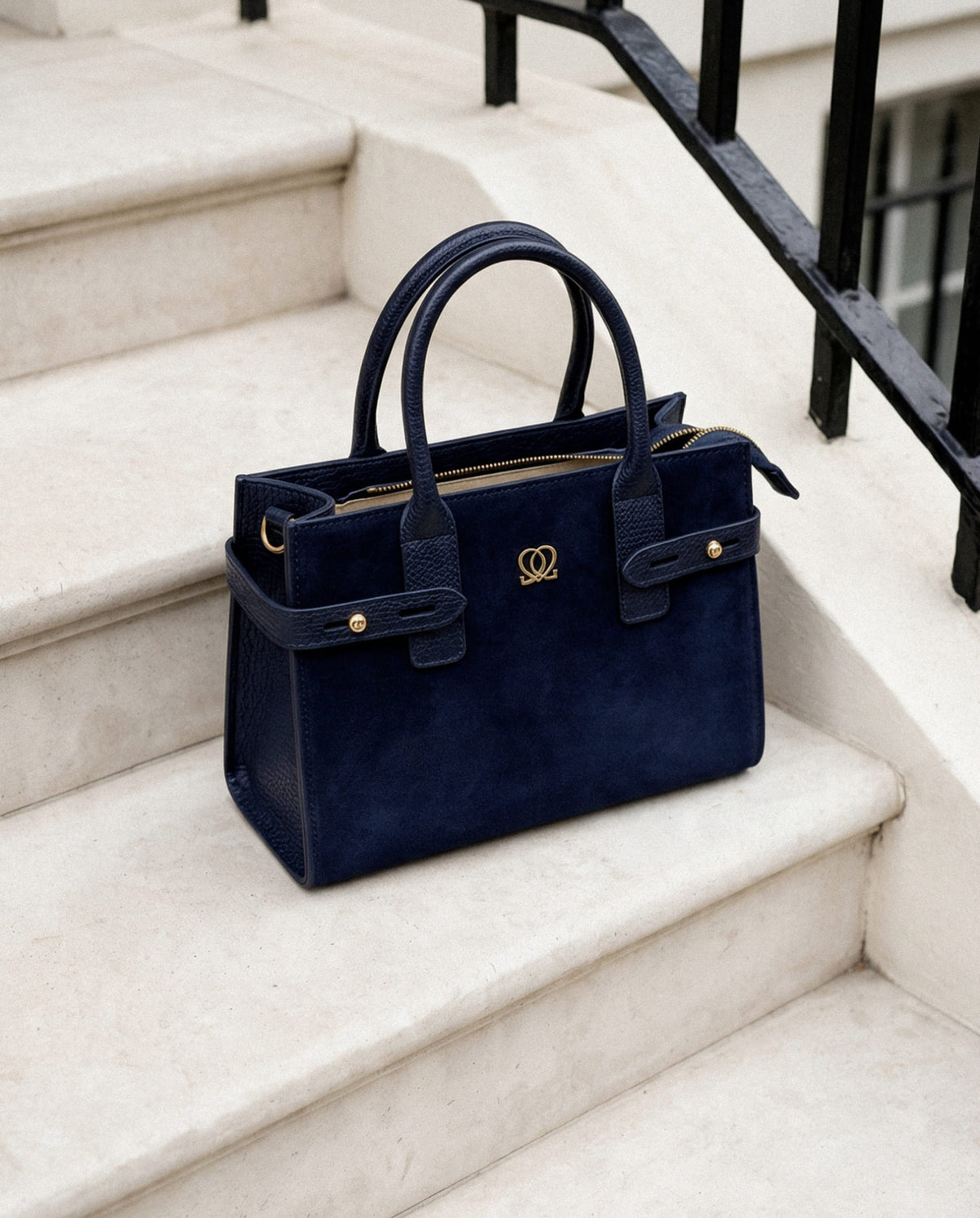 Classic Leather Handbag In Navy displayed on stone steps with top handles, gold-tone hardware and zip closure.