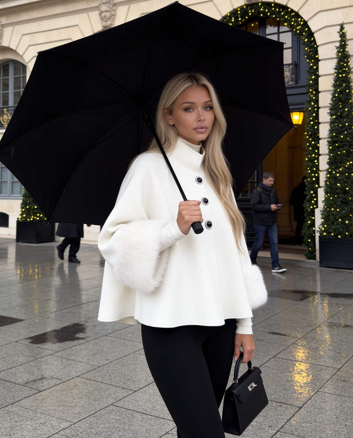 White knit poncho with faux fur cuffs worn with black trousers.