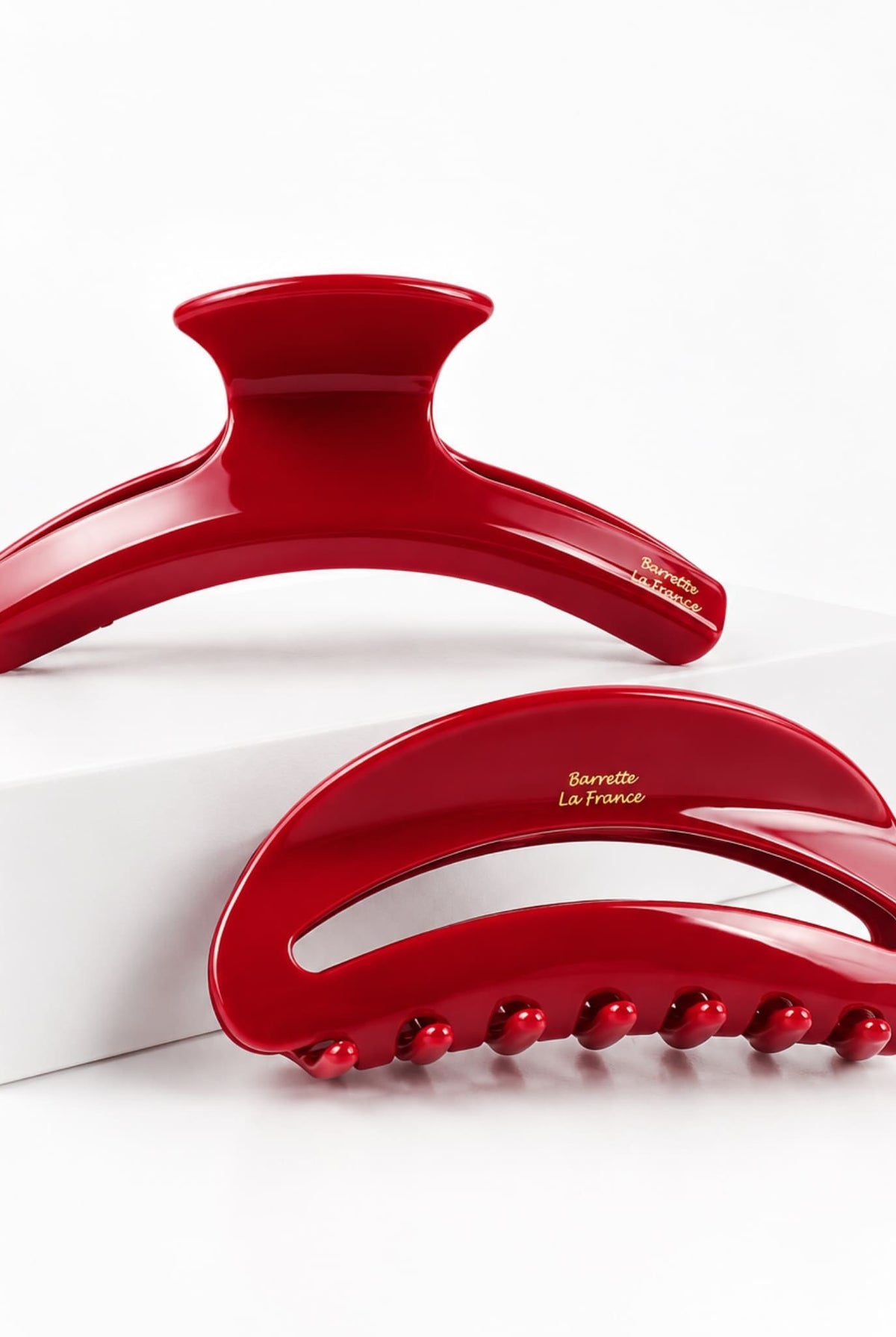 Set of two glossy red hair claw clips in curved designs with gold lettering, displayed on a white studio background.