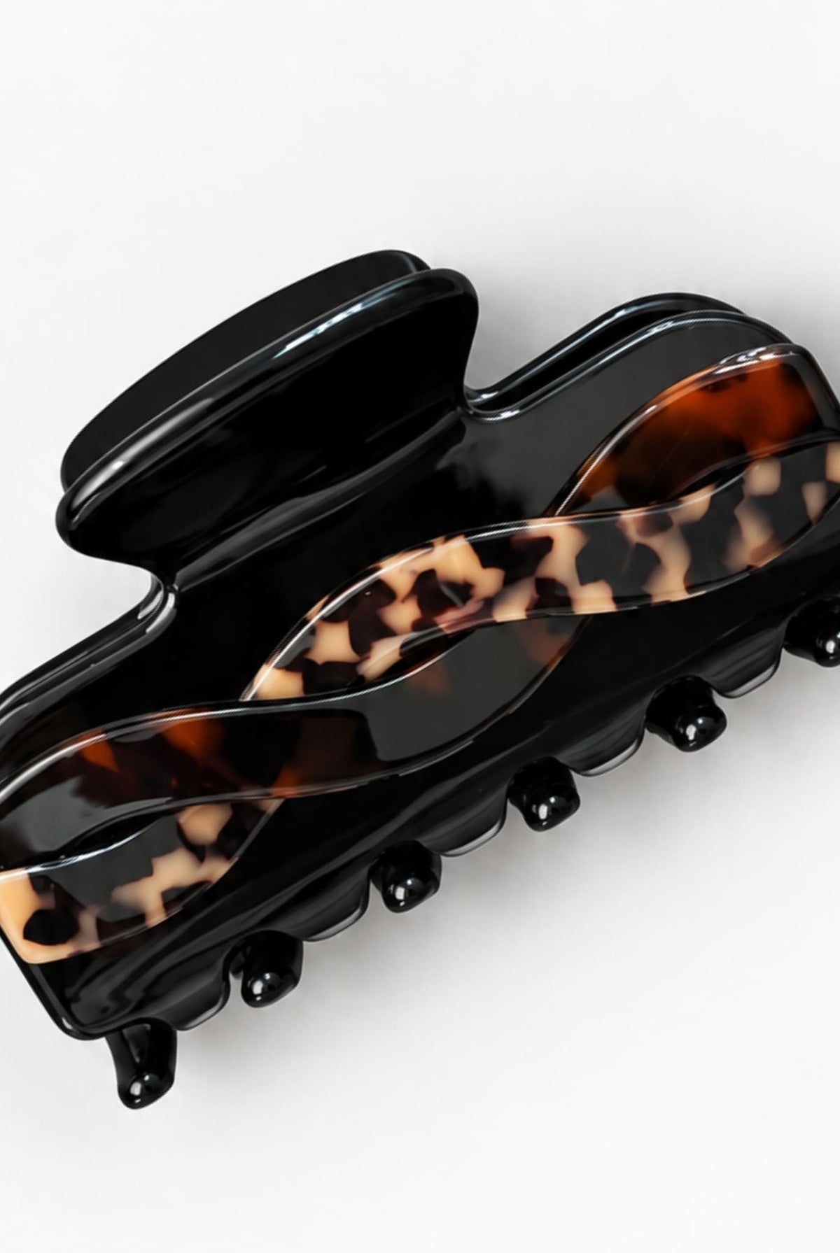 Glossy black hair claw clip with an intertwined tortoiseshell pattern in brown and beige, shown at an angle on a white background.