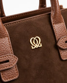 Close-up of Classic Leather Handbag In Brown showing brown suede-like material, textured handles, stitching and gold-tone emblem.