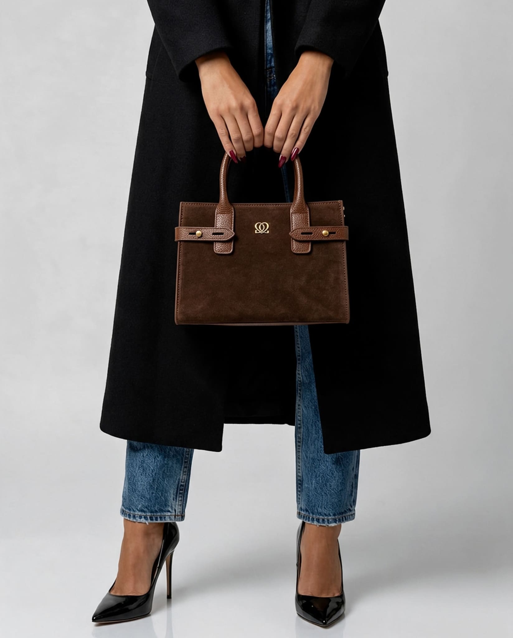 Classic Leather Handbag In Brown held by both handles, showing structured shape and gold-tone details.