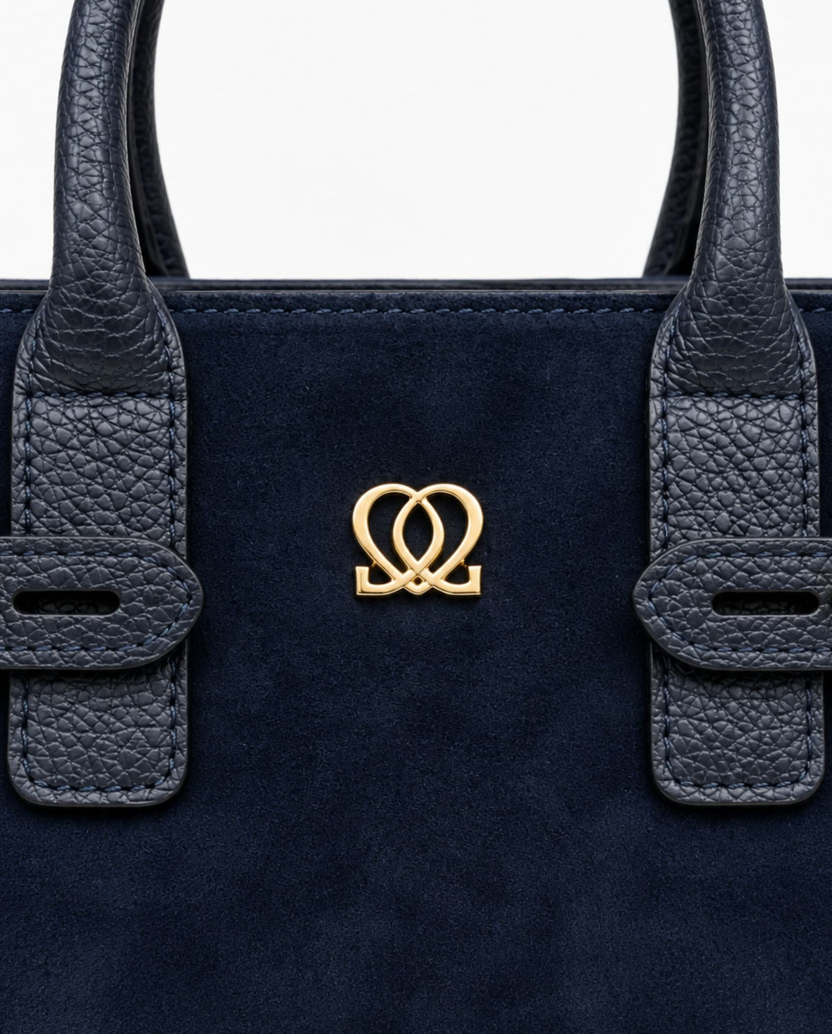 Close-up of navy handbag showing suede-like material, textured handle details and centered gold-tone emblem.