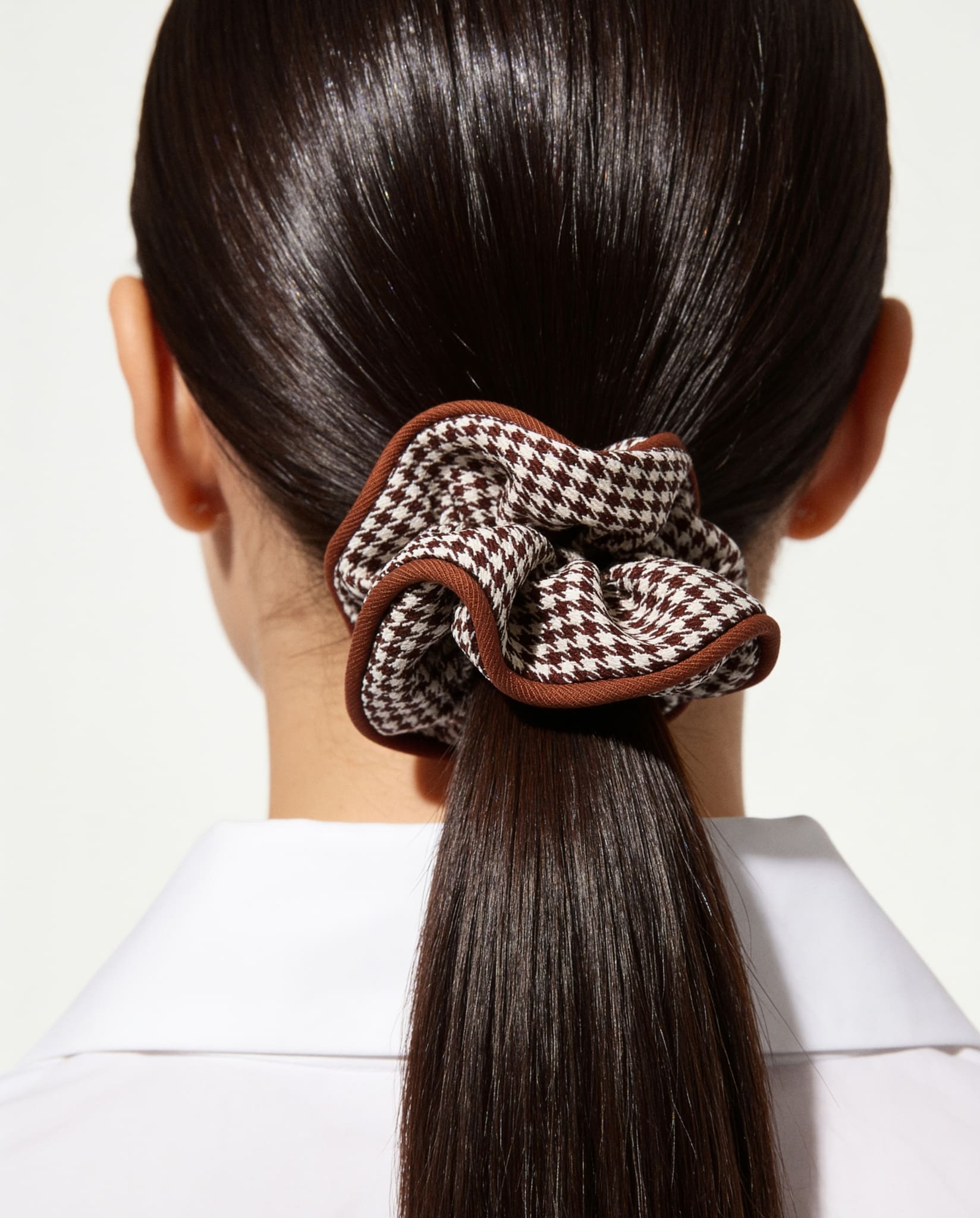 Houndstooth hair scrunchie in brown styled in a sleek ponytail.