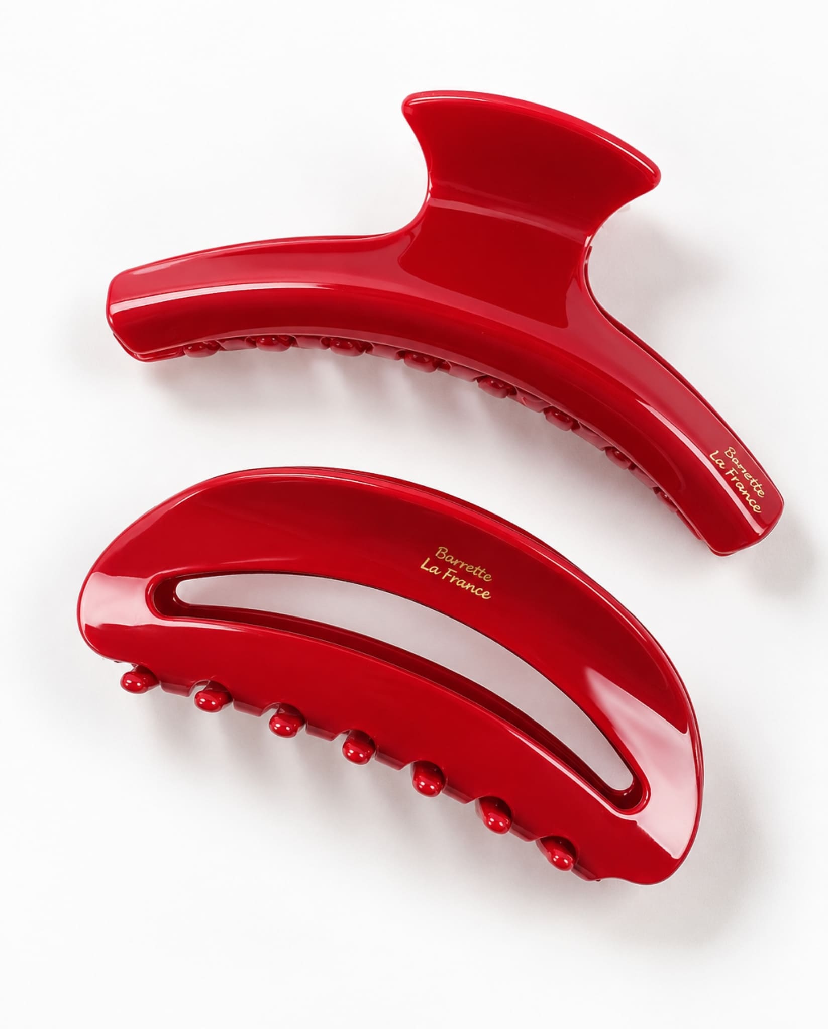 Two scarlet red hair claw clips with curved shapes, open cutout details and rounded teeth, viewed from above.