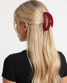Large red hair claw clip securing blonde hair in a half-up hairstyle, shown from the side.