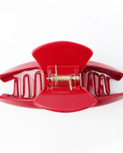 Close-up of an open red hair claw clip showing its curved teeth and metal spring mechanism.