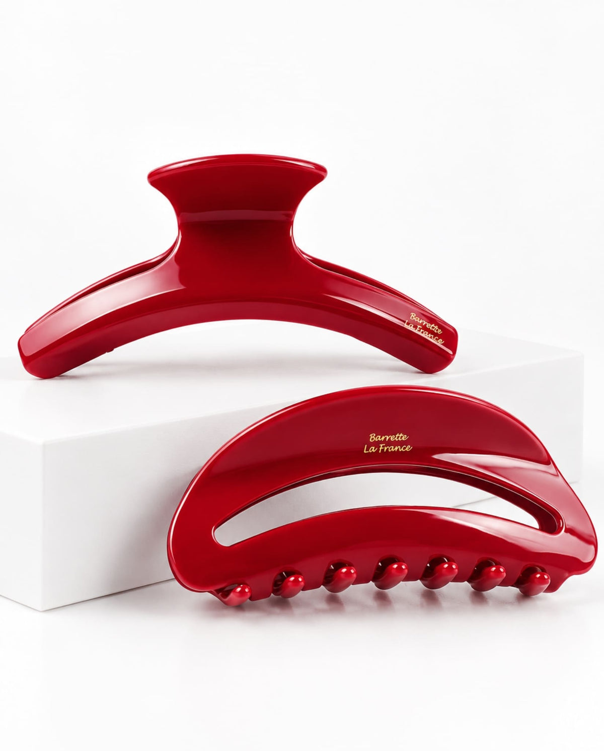 Set of two glossy red hair claw clips in curved designs with gold lettering, displayed on a white studio background.